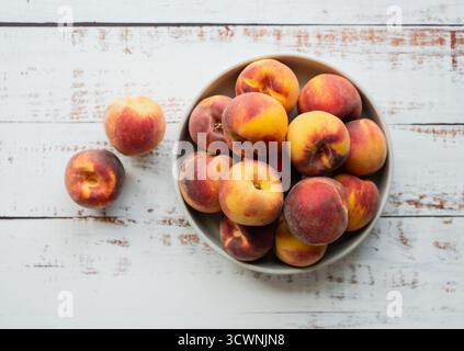 Top view of bowl of peaches on white wood background. Stock Photo