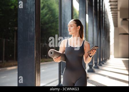 Woman in Activewear with Yoga Mat and Phone Outdoors Stock Photo