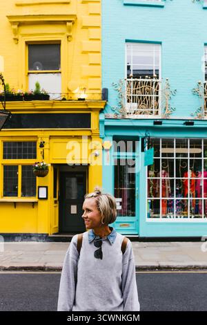 Woman smiles in front of bright yellow and aqua urban buildings Stock Photo