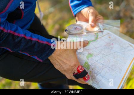 Orienteering athlete running through a summer forest with a map and compass. Close-up, selective focus on the map in his hands. Stock Photo