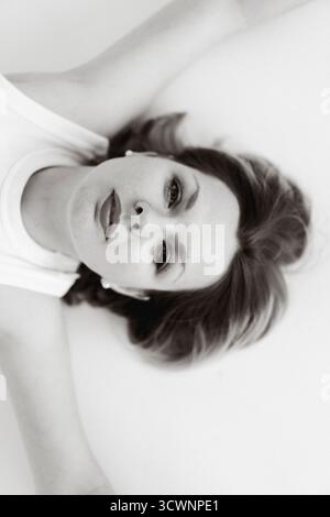 Portrait of a woman lying on a white surface looking at the camera Stock Photo