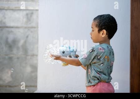 Asian toddler playing outside trying to catch floating bubbles from a bubble gun. Stock Photo
