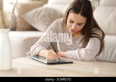Woman handwriting on digital tablet in the living room at home Stock Photo