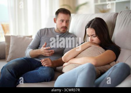 Sad woman and man explaining sitting on a couch at home Stock Photo