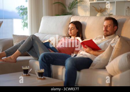 Couple at home reading paper books sitting on a couch at home Stock Photo
