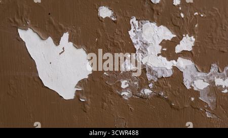 Close-up of a peeling painted wall, revealing layers of white and brown paint beneath. The textured surface and chipped paint create an abstract, weat Stock Photo