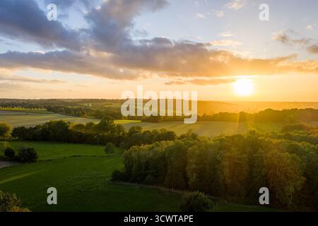 Golden Sunset Over Rolling Fields and Forest, Warm Light, Calm Rural Landscape at Dusk Stock Photo