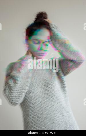 Mental health issue concept: grayscale portrait of a woman with hands on her head which is distorted in different color glitches Stock Photo
