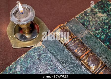 Close-up of an antique book titled “Oeuvres de Molière” with a marbled cover and gold-embossed spine, next to a lit candle in a brass holder. Stock Photo