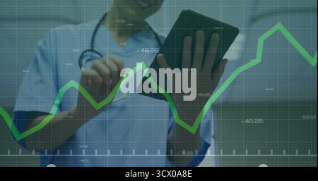 Tapping clinician in scrubs and stethoscope analyzing graph on tablet at clinic, with green overlay Stock Photo