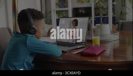 Watching boy wearing headphones using laptop at home dining area, with glass of juice, copy space Stock Photo