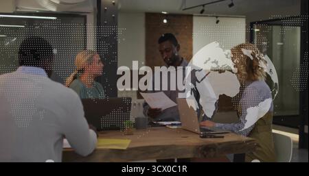 Reviewing printed documents, coworkers collaborating at table in office, with laptops, coffee mug Stock Photo