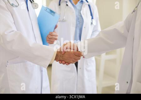 Two doctors in white lab coats shaking hands in clinic, symbolizing respect, teamwork and success. Stock Photo
