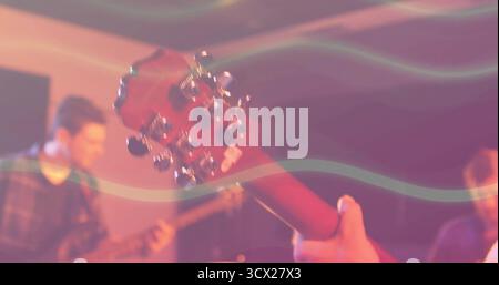 Framing musician holding headstock with chrome tuning pegs in rehearsal, stage lights creating haze Stock Photo