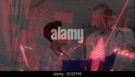 Reviewing stock-market charts, two doctors in treatment room using tablet computer and stethoscopes Stock Photo