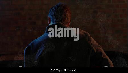Standing man wearing dark canvas jacket against brick wall in studio, with colored accent lighting Stock Photo