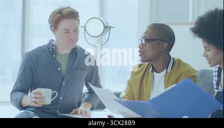Team of three professionals discussing project plans in office lounge, with mugs and blue binder Stock Photo