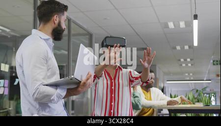 Reaching woman wearing VR headset exploring demo in modern office, with silver laptop and plant Stock Photo