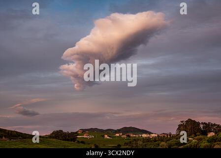 Dramatic isolated cloud over the rural hills and village of Miengo, Cantabria, northern Spain, at dusk Stock Photo