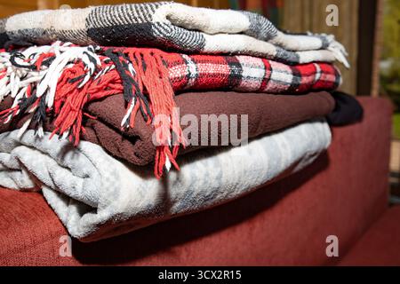 Neatly folded blankets with soft textures and warm colors on red sofa symbol of comfort home care and cozy living Stock Photo