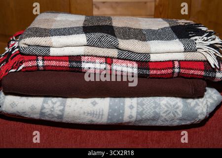 Neatly folded blankets with soft textures and warm colors on red sofa symbol of comfort home care and cozy living Stock Photo