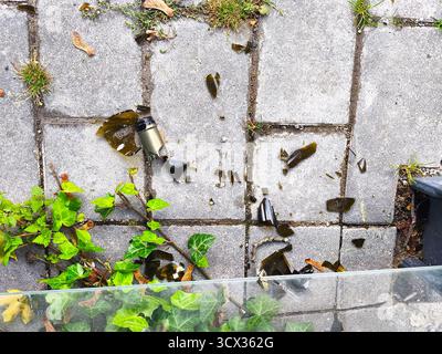 Broken glass bottle shards on a gray paved urban sidewalk Stock Photo