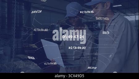 Coworkers wearing coveralls analyzing timestamped overlays in warehouse using laptop and smartphone Stock Photo