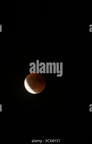 Moon passing through a partial lunar eclipse, casting an orange red shadow Stock Photo