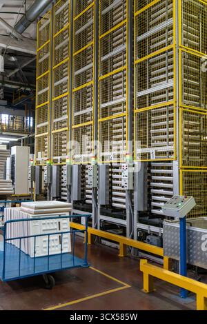 A modern automated factory for refrigerator production, featuring an industrial storage system with insulation panels stacked inside. A cart with pane Stock Photo