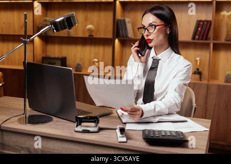 Professional businesswoman checks documents and speaks by phone while working on finance at office desk Stock Photo