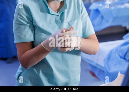 Closeup nurse in scrubs putting on sterile gloves before a procedure, showing aseptic PPE, infection control, and patient safety in the OR. Stock Photo
