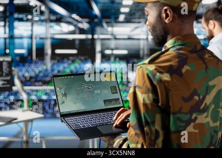 Black military IT expert in server hub using AI tools to oversee battlefield surveillance to develop warfare tactics. Army data center admin doing transmission analysis and live monitoring. Stock Photo
