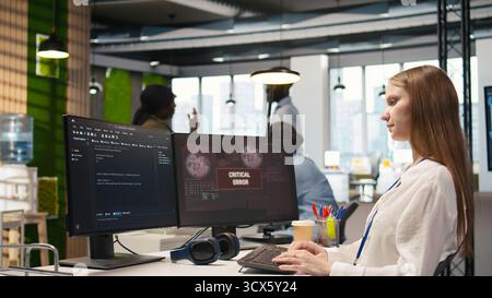 Young inexperienced developer in office struggling to fix critical error warning popup. Intern troubleshooting error notification on computer screen interrupting workflow, camera A Stock Photo