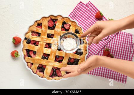 Woman adding sugar powder onto tasty berry pie on white background Stock Photo