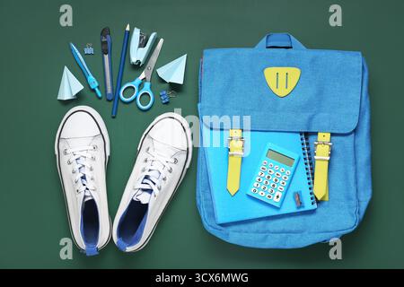 Different stationery with backpack and stylish sneakers on green background Stock Photo