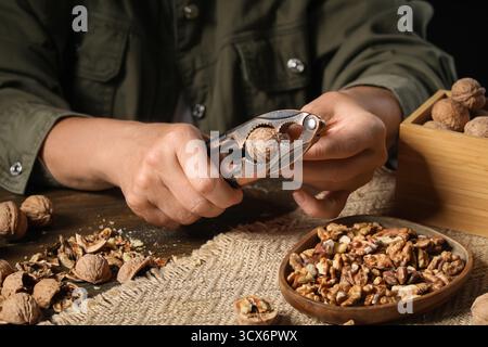Woman cracking walnuts with nutcracker on wooden table Stock Photo