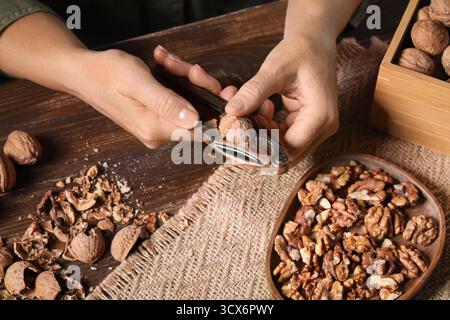 Woman cracking walnuts with nutcracker on wooden table Stock Photo