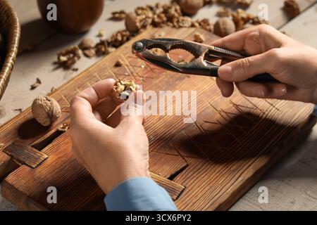 Elderly woman cracking walnuts with nutcracker on wooden table Stock Photo