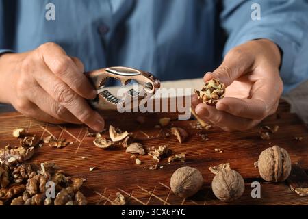 Elderly woman cracking walnuts with nutcracker on wooden board Stock Photo