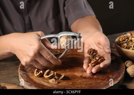 Elderly woman cracking walnuts with nutcracker on wooden table Stock Photo