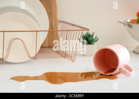 Overturned cup and spilled coffee on counter in kitchen, closeup Stock Photo