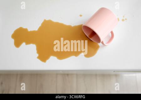 Overturned cup and spilled coffee on counter in kitchen, top view Stock Photo