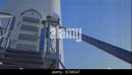 Holding open laptop, construction worker in hard hat comparing data on tower platform with railing Stock Photo