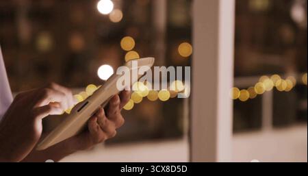 Tapping hands in white long-sleeve shirt on white tablet inside room, with bokeh lights, copy space Stock Photo