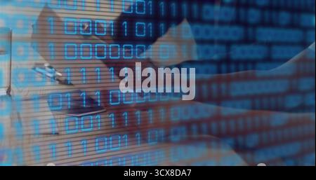 Man wearing button up shirt writing in notebook, typing on laptop at workspace, binary code overlay Stock Photo