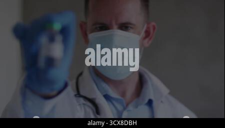 Offering male doctor holding small glass vial in clinic, wearing lab coat stethoscope mask gloves Stock Photo