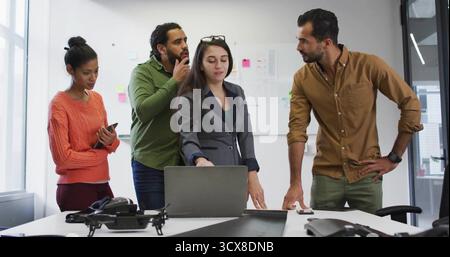 Gesturing lead in grey blazer directing discussion at meeting room, with laptop and drone prototype Stock Photo