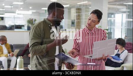 Discussing designers in shirts and blouses reviewing schematics in office lounge with laptop Stock Photo