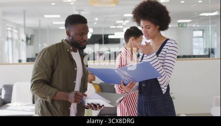 Reviewing paperwork, two team members collaborating in office lounge, with blue folder, clipboard Stock Photo