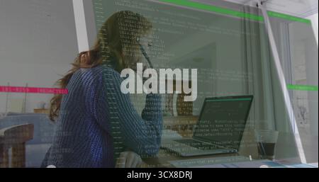 Leaning woman programmer studying laptop screen at modern office, with coffee cup and code overlay Stock Photo